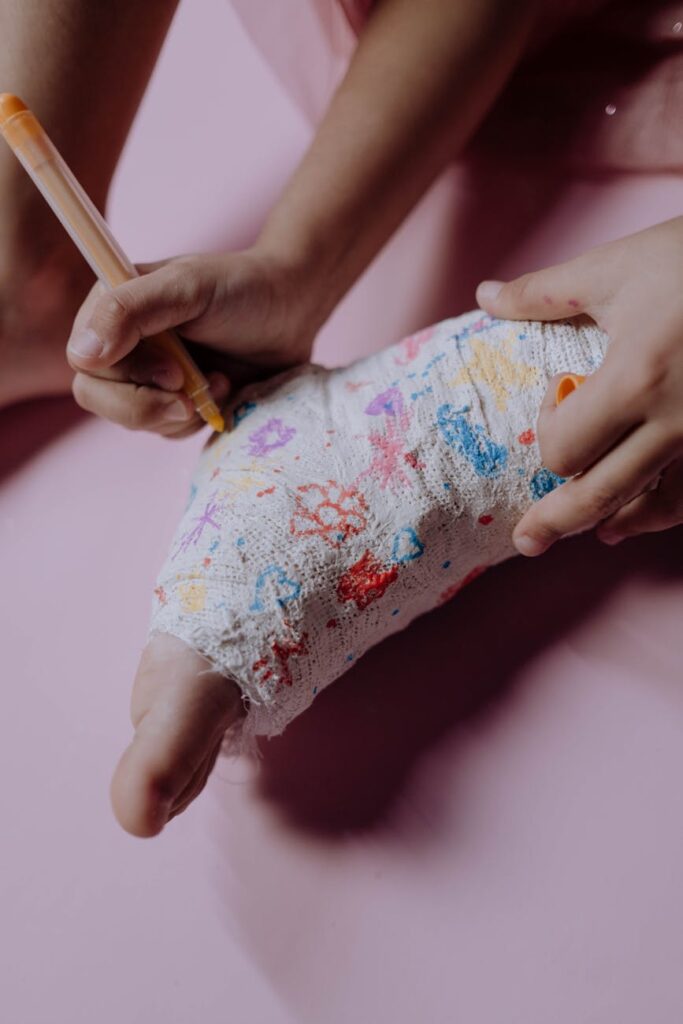 A child's hands drawing on an orthopedic cast with colored pens on a pink background.